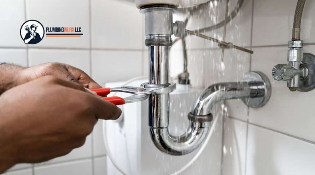 Hands using a red wrench to tighten a leaking chrome pipe underneath a sink with water spraying out, indicating urgent plumbing repair.
