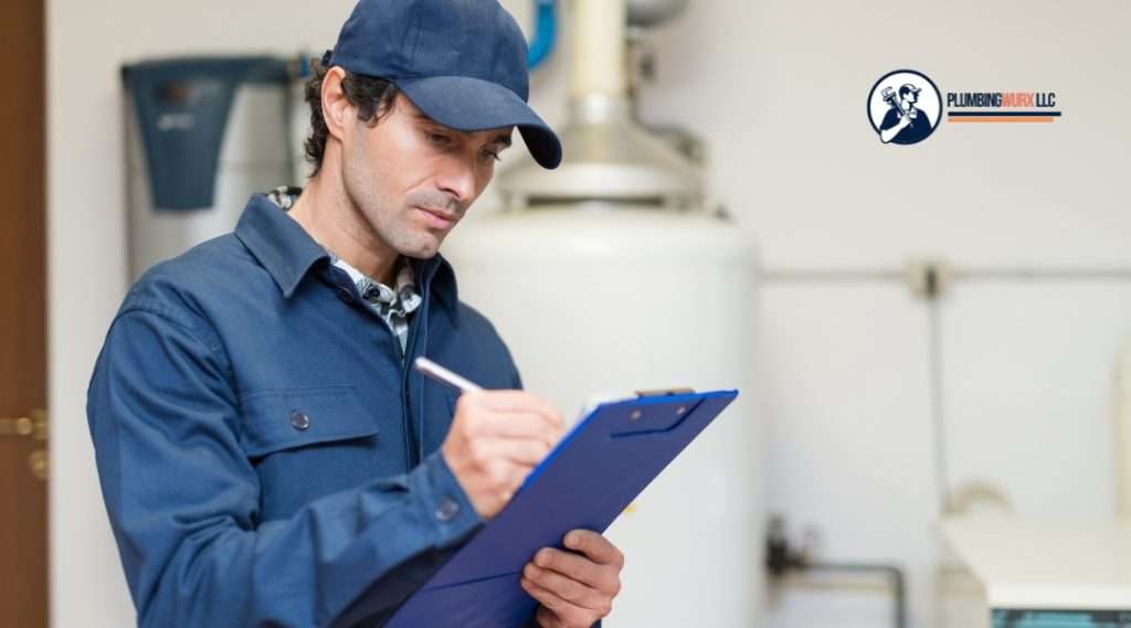 A plumber in a blue uniform and cap writes on a clipboard while standing in front of a water heater, documenting inspection or service details.