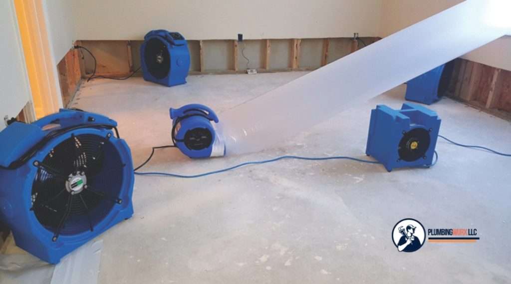  Multiple blue air movers and dehumidifiers drying a stripped-down room after water damage.