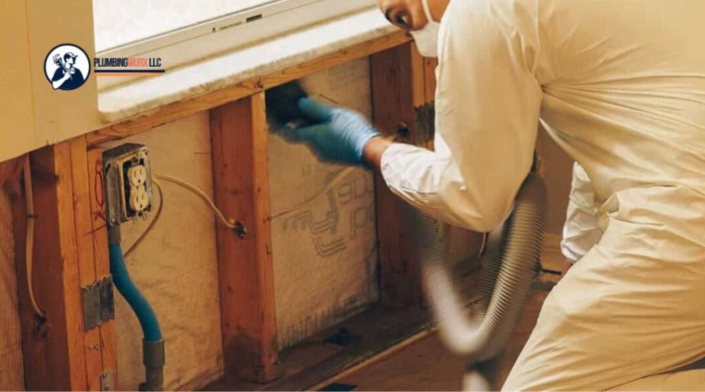Worker in protective gear vacuuming inside exposed wall cavities for water damage cleanup.